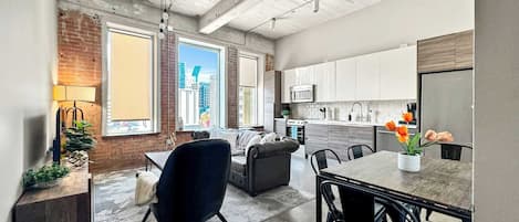 A modern kitchen with white cabinets, a stainless steel refrigerator, and a dining area with a table and chairs.