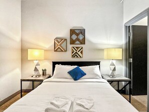 A hotel room with a large bed, two bedside tables, a black headboard, and wall-mounted artwork.