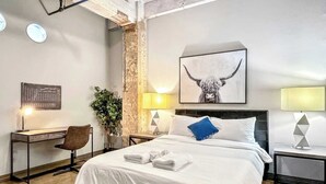 Habitación de hotel con una cama grande, un escritorio, una silla, una planta en maceta y una obra de arte en la pared.