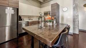 A modern kitchen with stainless steel appliances, a wooden dining table, and a clock on the wall. - Elegant 3BD | DT Dallas | Sleeps 9 | ValetParking (Dallas)