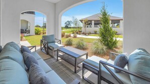Un patio con sofá, sillas y mesa, con vistas a un jardín y una casa.
