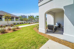 A residential area with a well-maintained lawn, a patio with outdoor furniture, and a pool in the background.