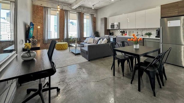 A modern kitchen with stainless steel appliances, a dining area with a table and chairs, and a living space with a sofa and a coffee table.