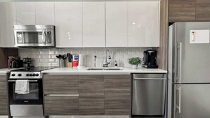 A modern kitchen with a stainless steel refrigerator, a built-in oven, a microwave, and a sink with a wooden countertop.