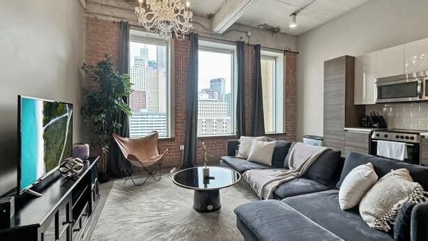 A modern living room with a large sofa, a coffee table, a TV, and a city view through large windows.