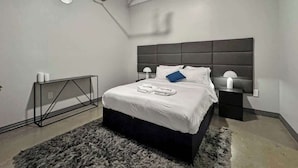 A modern bedroom with a large bed, a console table, and a nightstand.