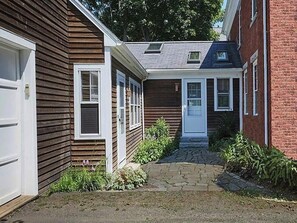 Een smal pad dat leidt naar een huis met een voordeur, een garage en een klein portaal met planten.