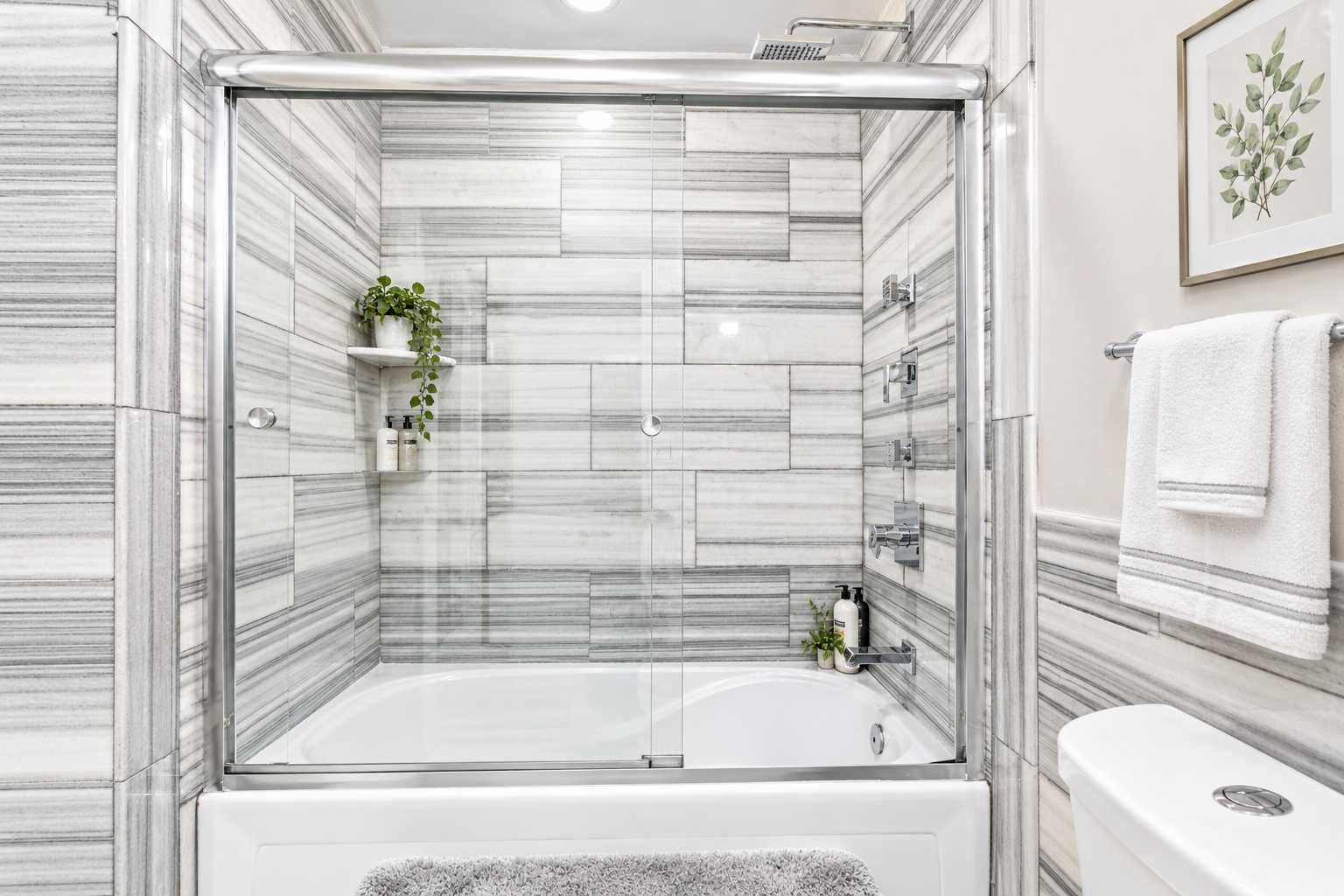 A modern bathroom with a glass-enclosed shower, a white bathtub, and a toilet.