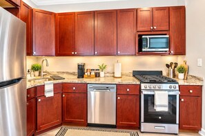 A modern kitchen with wooden cabinets, stainless steel appliances, and a granite countertop. - Luxury Studio | 2 Beds | Northern Liberties (Philadelphia)