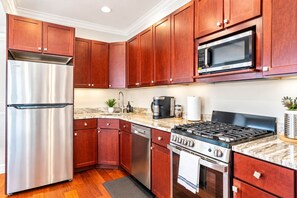 A kitchen with wooden cabinets, stainless steel appliances, a microwave, a coffee maker, and a stove. - Luxury Studio | 2 Beds | Northern Liberties (Philadelphia)