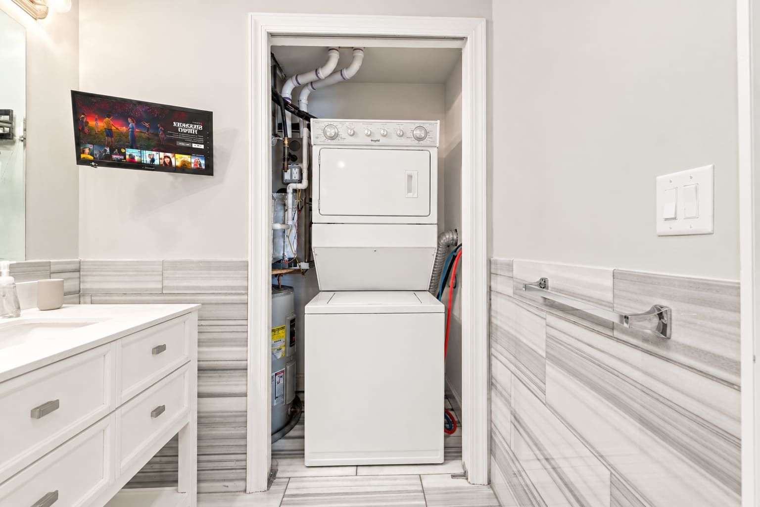 A compact laundry room with a washer and dryer, a tiled floor, and a wall-mounted television.