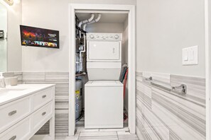 A compact laundry room with a washer and dryer, a tiled floor, and a wall-mounted television. - Luxury Studio | 2 Beds | Northern Liberties (Philadelphia)