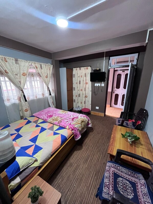A hotel room with a bed, a desk with a chair, a TV, and a door leading to another room. - Zimba Happy Home Stay (Darjeeling)