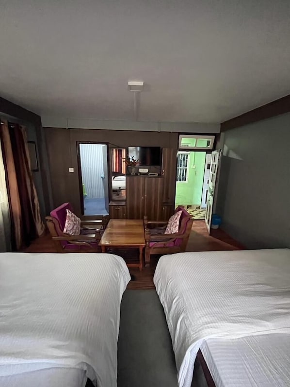 A hotel room with two beds, a small table, a TV, and a view of the outside.
