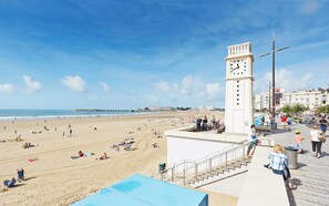 Uma praia com uma torre do relógio, uma passarela e vista para o mar.
