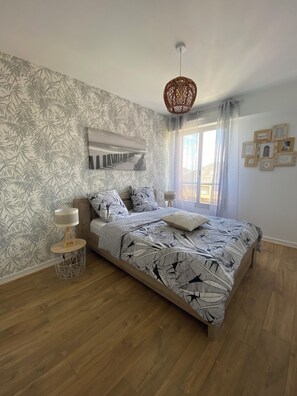 Quarto com cama, papel de parede estampado, luminária pendente e janela com cortinas.