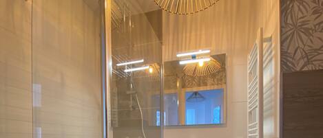 A modern bathroom with a glass shower enclosure, a white sink, and a mirror above it.
