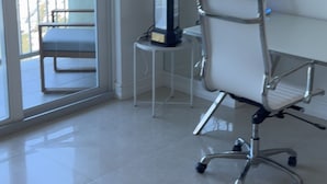 Ein moderner Arbeitsraum mit großem Schreibtisch, einem Sessel, einer Stehlampe und Meerblick vom Balkon.