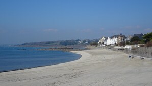 A wide sandy beach with a clear blue sky, a few people walking, and houses in the background. - Stone House by Beach in Pont-aven (Tregunc)