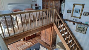 A loft-style room with a high ceiling, a wooden staircase, a blue sofa, a patterned rug, and a wooden cabinet with decorative elements. - Stone House by Beach in Pont-aven (Tregunc)
