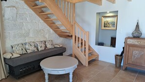 A cozy living room with a wooden staircase, a sofa with patterned cushions, a round table, and a cabinet. - Stone House by Beach in Pont-aven (Tregunc)