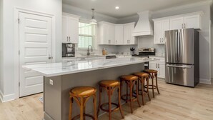 A modern kitchen with white cabinetry, a stainless steel refrigerator, a large island with stools, and a built-in oven. - NEW! "Days Like This" 5/5, Private POOL, Sleeps 14, Easy Gulf Beach Access (Dauphin Island)