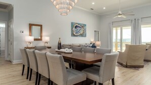 A spacious dining room with a large wooden table, several upholstered chairs, a chandelier, and a painting on the wall. - NEW! "Days Like This" 5/5, Private POOL, Sleeps 14, Easy Gulf Beach Access (Dauphin Island)