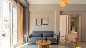 A modern living room with a grey sofa, a wooden coffee table, and two framed artworks on the wall. - 2BD Modern Home Steps from Pasalimani (Pireas)