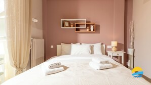 A hotel room with a bed, a bedside table with a lamp, a wall-mounted shelf with decorative items, and a radiator. - 2BD Modern Home Steps from Pasalimani (Pireas)