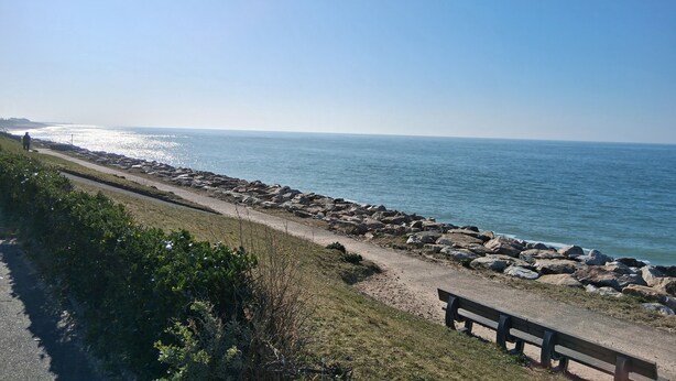 A coastal walkway with a bench, a rocky shoreline, and a clear view of the sea. - The RIVA A 207 (Barneville-Carteret)