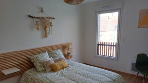 A bedroom with a bed, a window, a wall-mounted macrame decoration, and a green chair. - The RIVA A 207 (Barneville-Carteret)