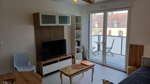A living room with a television, wooden cabinets, a dining table, and a sofa. - The RIVA A 207 (Barneville-Carteret)