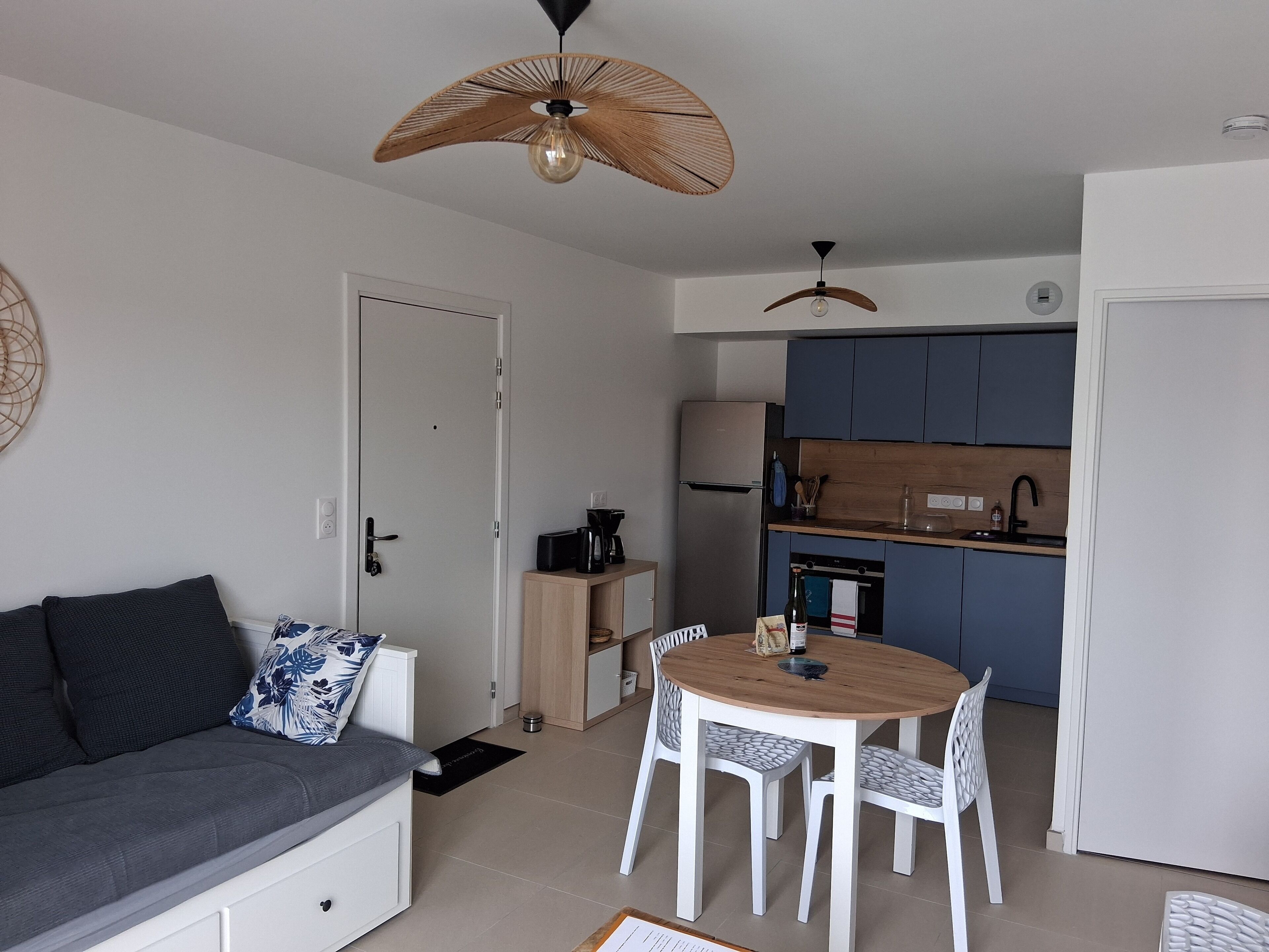 Ein kompakter Wohnraum mit Sofa, Esstisch, Stühlen, einer Küchenzeile inklusive Schränken und Deckenventilatoren.