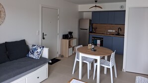 A compact living space with a sofa, dining table, chairs, a kitchen area with cabinets, and ceiling fans. - The RIVA A 207 (Barneville-Carteret)