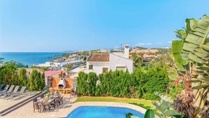 Eine Villa mit Swimmingpool, Sitzgelegenheiten im Freien und Meerblick.