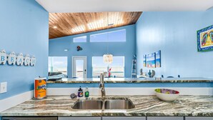 A kitchen with a wooden ceiling, blue walls, a marble countertop, a sink, and a dishwasher. - Beach Blast: Gulf-Front 3bd/2ba on North Cape - Ocean Views From Every Room (Port St. Joe)