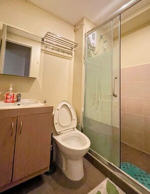 Baño con inodoro, lavabo y cabina de ducha de vidrio.