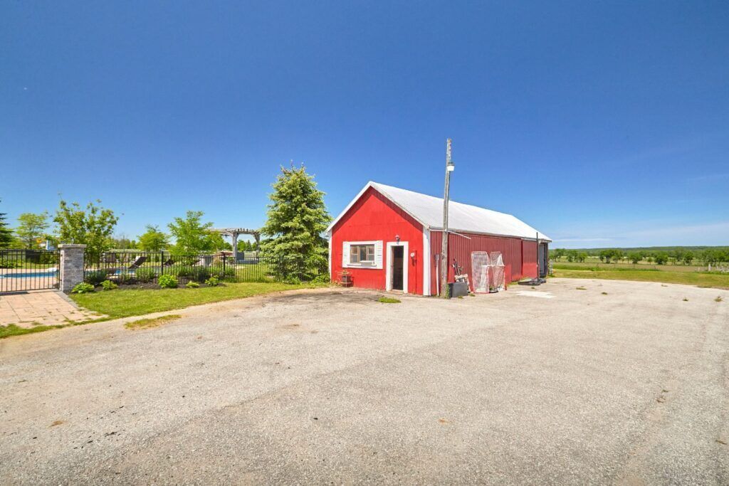 A red building with a white roof, a gravel driveway, and a metal fence.