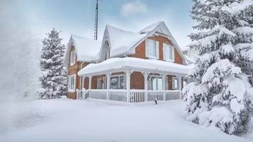 A snow-covered house with a porch and a chimney.