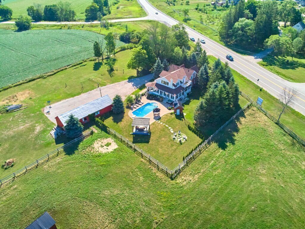 Vista aérea de una casa grande con piscina, rodeada por un patio cercado y una calle.