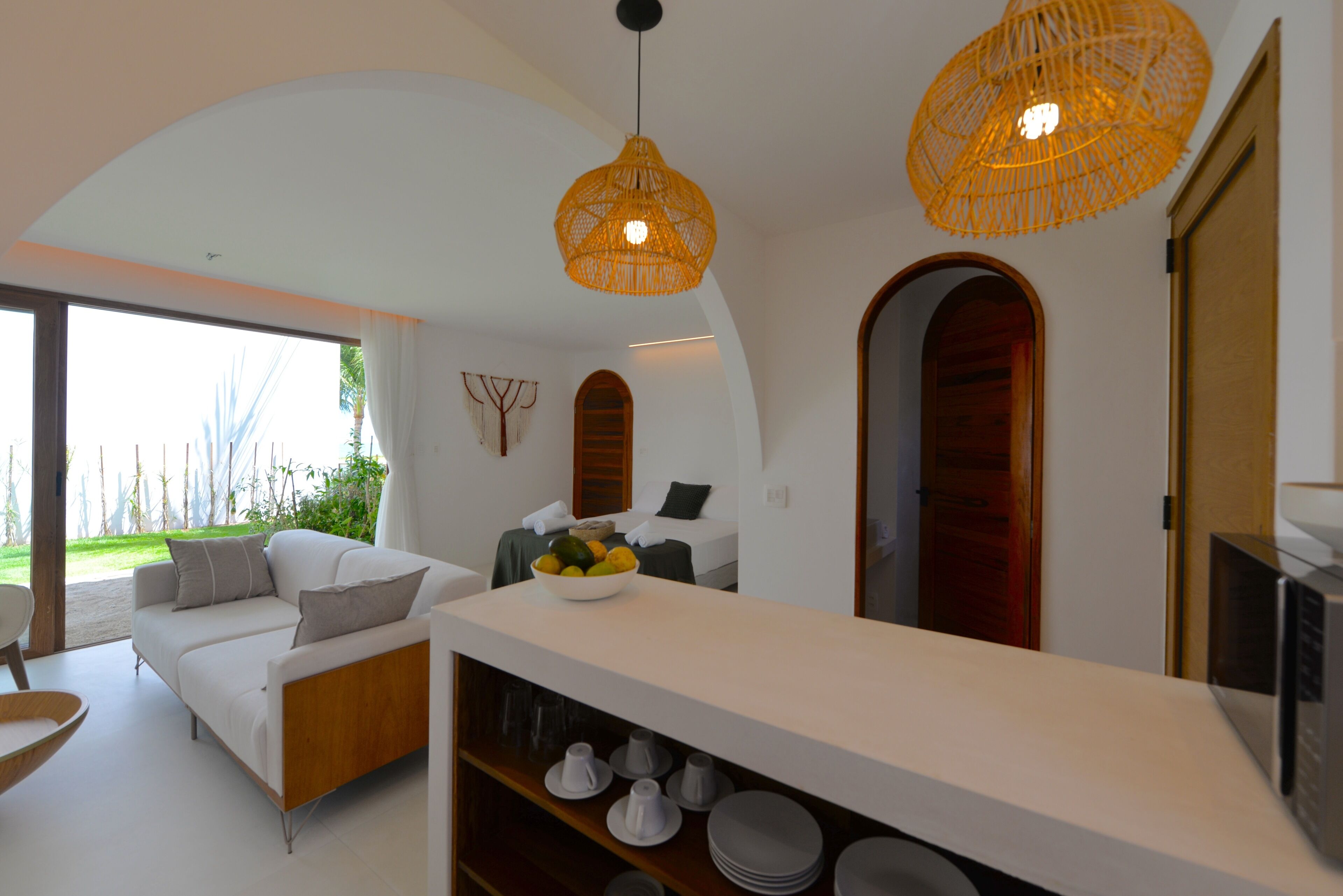A modern living room with a sofa, a dining table with a fruit bowl, and a kitchen area with a microwave.