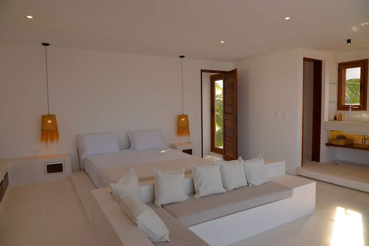 Een moderne slaapkamer met een groot bed, nachtkastjes, een bank en een raam met uitzicht.