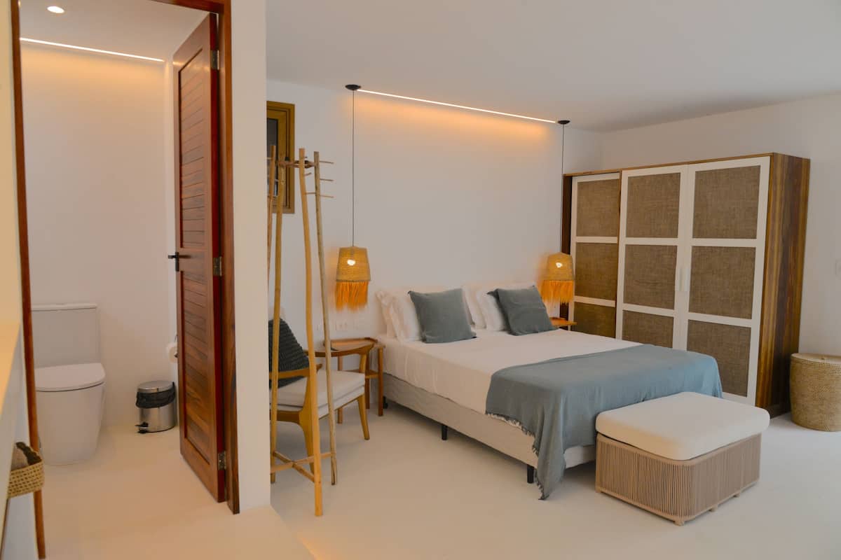 Een slaapkamer met een bed, nachtkastjes, een kledingkast, een stoel en een kleine prullenbak.
