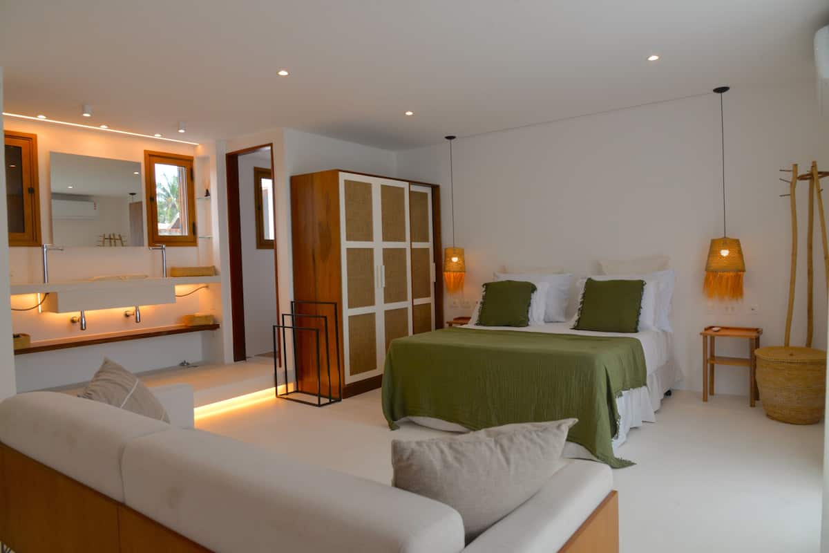 Een moderne slaapkamer met een groot bed, een bank, een garderobe en een spiegel.