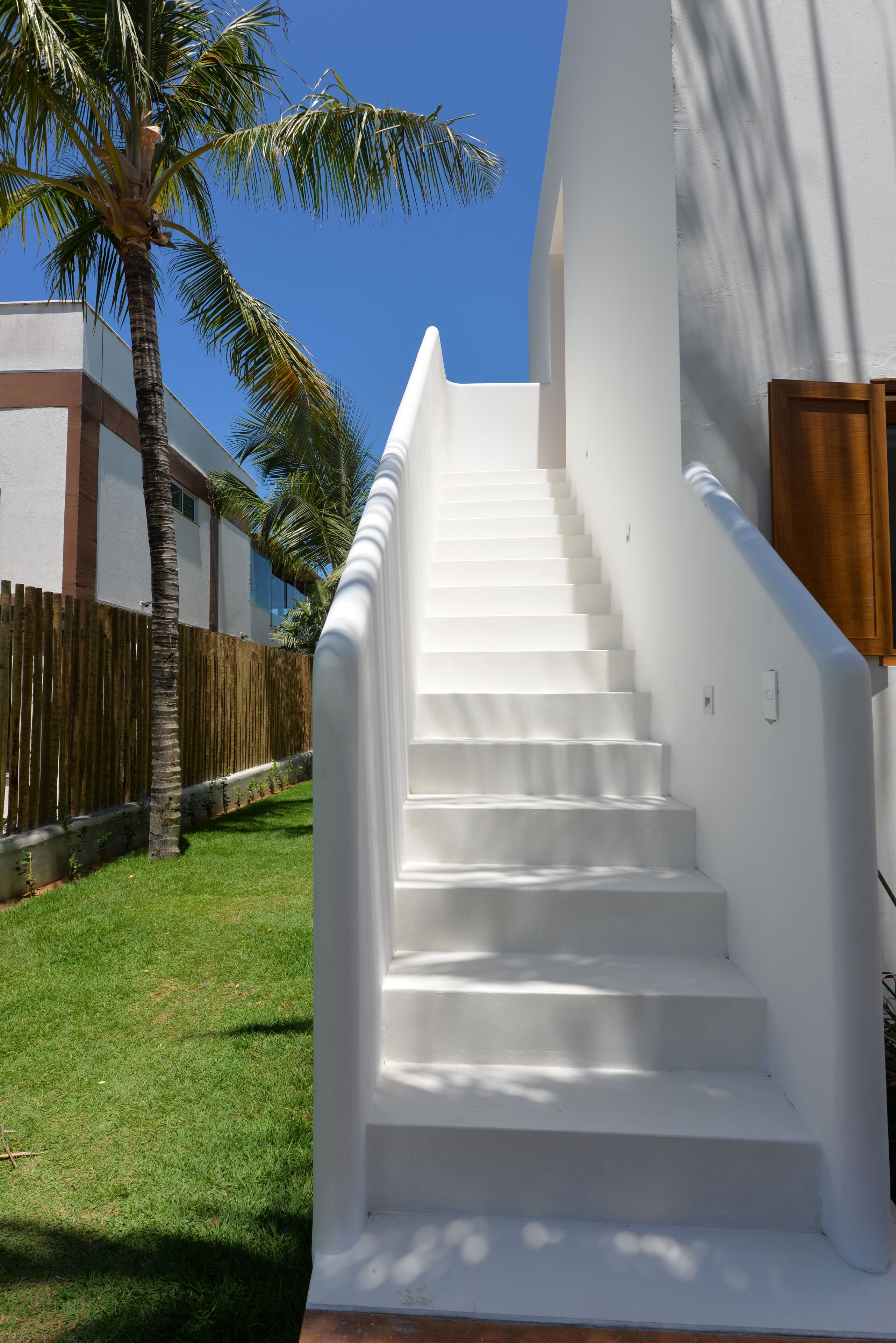 A white staircase leading to a building with a wooden fence and a palm tree in the background.