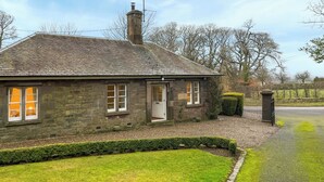 A stone house with a tiled roof, a chimney, and a well-maintained lawn.