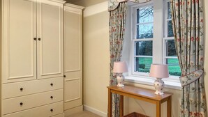 A bedroom with a bed, a wardrobe, a window with curtains, and a bedside table with lamps and a basket.