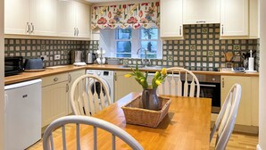 A kitchen with white cabinets, a wooden dining table, and chairs. There is a washing machine, a microwave, and a sink.