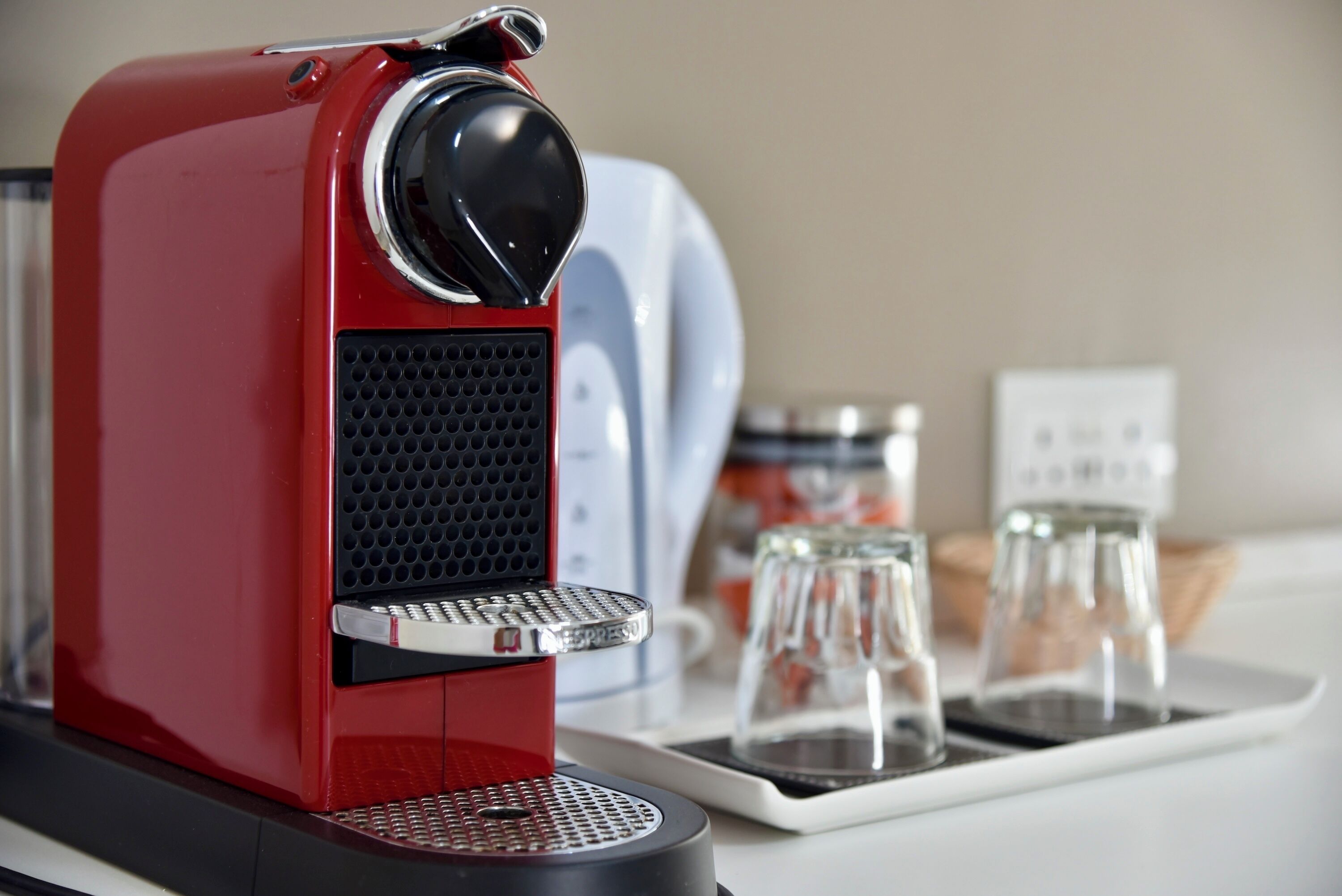 Una máquina de espresso roja con un molinillo de café, una cafetera blanca y una bandeja con dos jarrones de vidrio.