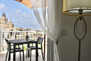 A balcony with a table and chairs, a lamp, and a view of a cityscape with domed buildings. - Alight Sauna and SPA Penthouse (Xewkija)